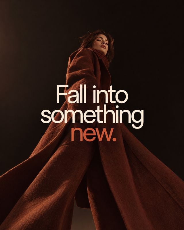 rust-brown coat autumn product photo: A model poses in a sweeping rust-brown coat against a dark studio backdrop, lit with warm dramatic light beneath the head…