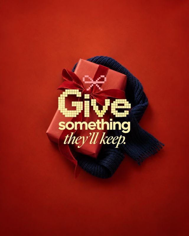 scarf still life product photo: A red gift box tied with a bow rests on a dark knitted scarf against a deep red studio backdrop, with warm golden headline typo…