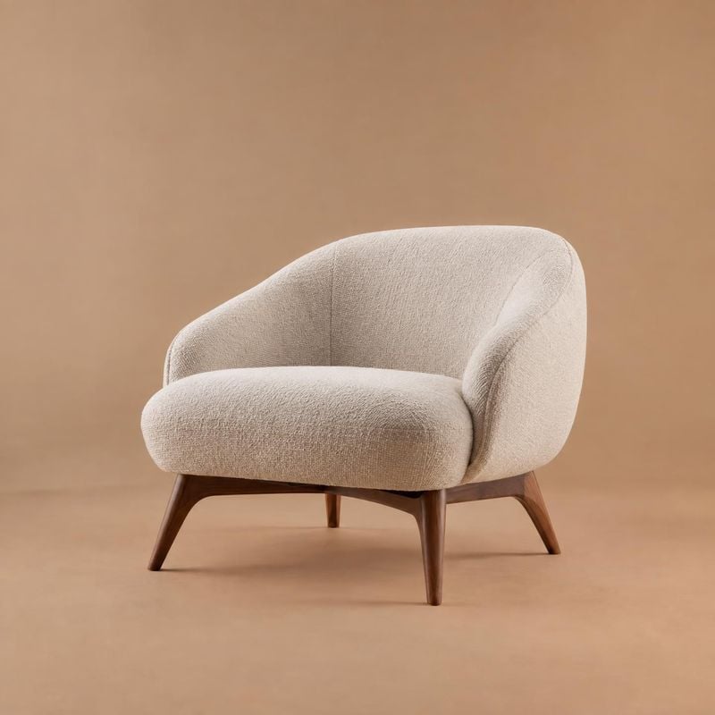 upholstered accent chair home product photo: A cream upholstered accent chair with tapered walnut legs is isolated against a warm tan studio backdrop, lit soft…