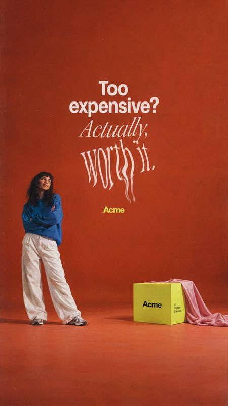 yellow product box still life product photo: An adult woman in a blue top and loose white trousers stands beside a yellow box and draped pink fabric in a warm…