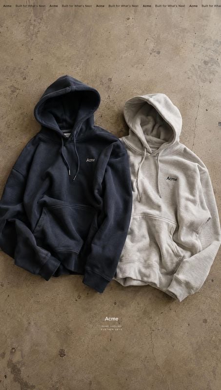 hoodies flat lay product photo: Two hoodies in dark navy and light gray lie side by side on a textured concrete surface, with soft overhead light and a restrai…