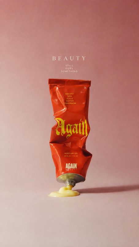 moisture gel packshot product photo: A crumpled red moisture-gel tube stands open on a soft pink studio backdrop, with a small pool of yellow gel and restraine…