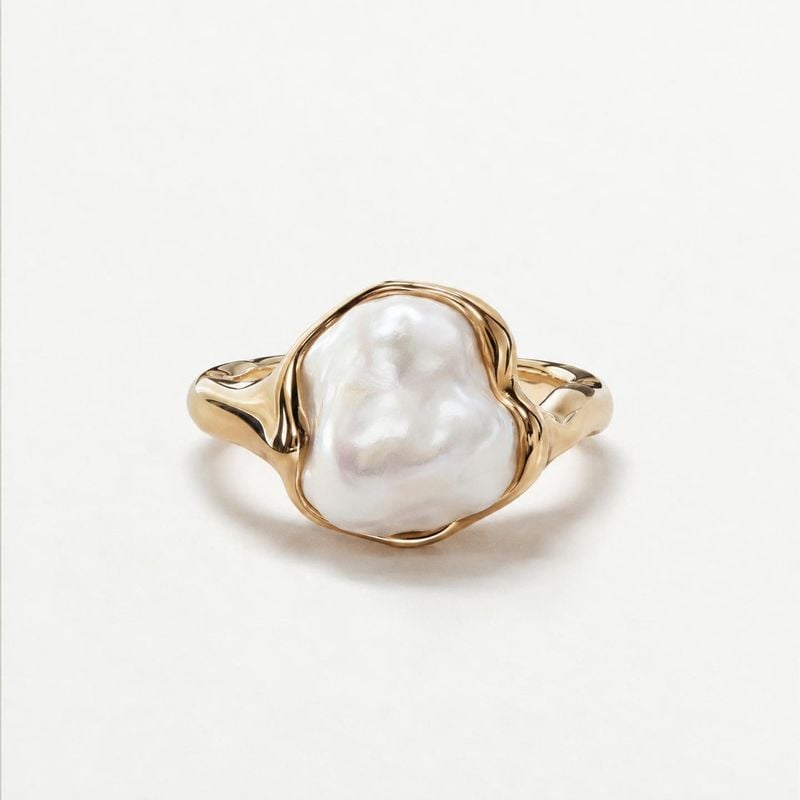 pearl ring jewelry product photo: A sculptural gold-tone ring with a large irregular white pearl is centered on a clean white background, lit softly for a poli…