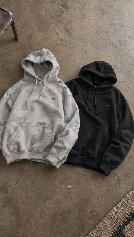 hoodies flat lay product photo: Two gray and black hoodies are arranged side by side on a rough concrete floor, with small lettering on the garments and unders…