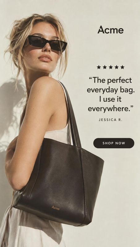 tote bag on-body detail product photo: A woman in a light sleeveless dress and dark sunglasses models a large black tote against a warm off-white backdrop, wit…