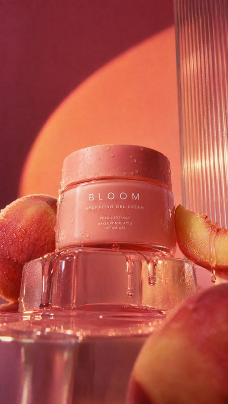 hydrating gel cream ingredients product photo: A pink gel cream jar sits on a reflective surface among ripe peaches, with water droplets and warm coral lightin…