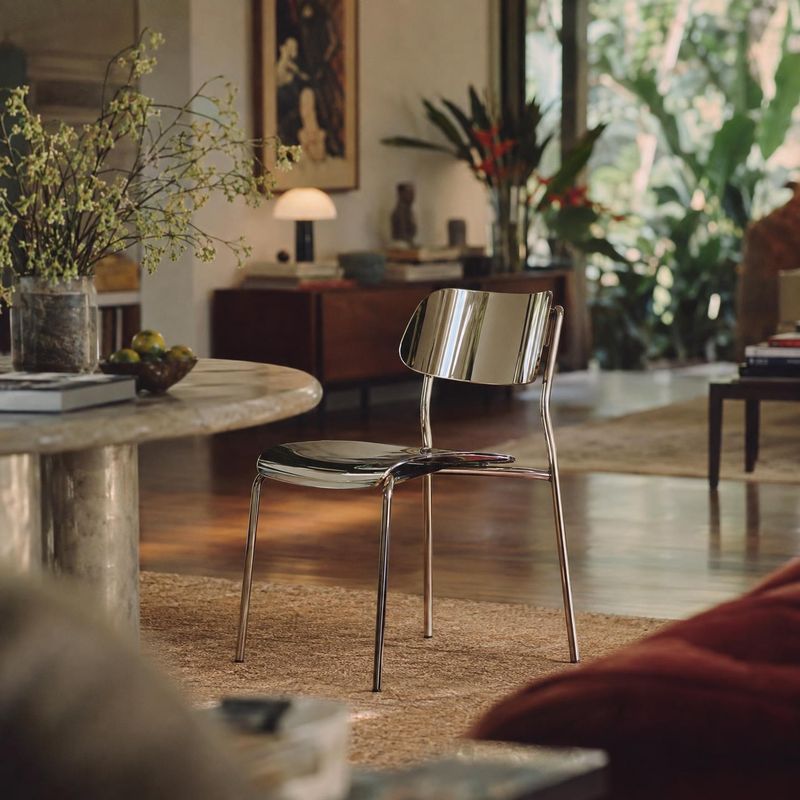 chrome dining chair room set product photo: A polished chrome chair sits amid warm wood floors, a round stone table, plants and softly lit furnishings, creatin…