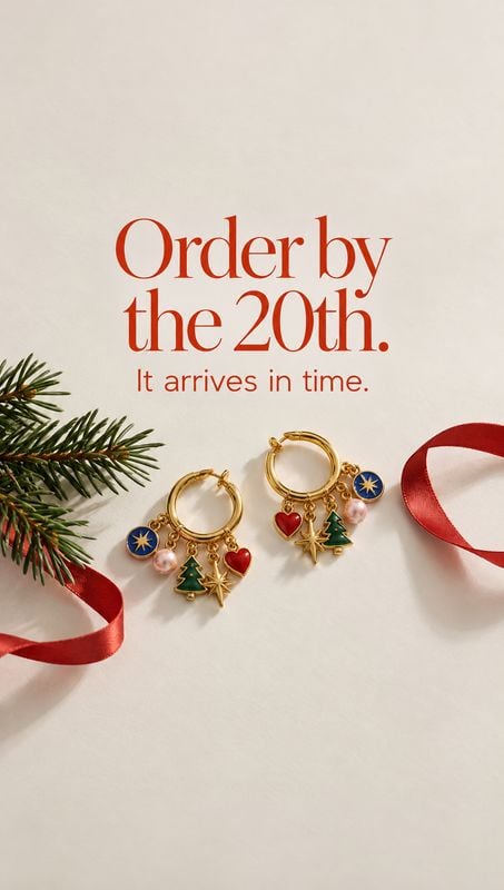 holiday charm hoop earrings christmas product photo: Gold hoop earrings with colorful festive charms are arranged on a cream surface with evergreen sprigs and…