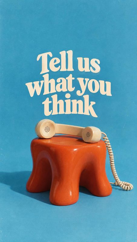 telephone handset electronics product photo: A cream vintage telephone handset rests on a glossy orange stool against a vivid blue studio backdrop, beneath ove…