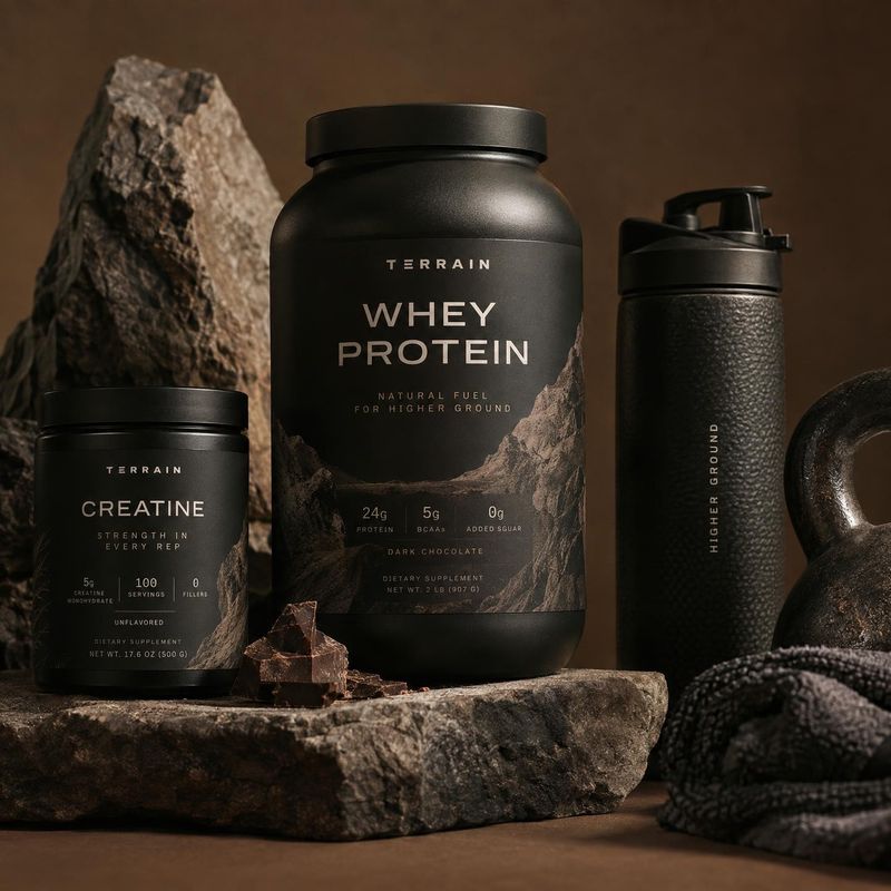 protein powder and creatine supplements personal care product photo: Black supplement containers and a shaker are arranged among rugged rocks and textured fabr…
