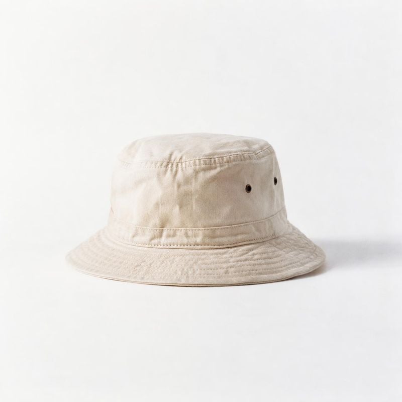 bucket hat fashion product photo: A light beige cotton bucket hat is centered against a clean white studio background, softly lit for a simple product-focused…