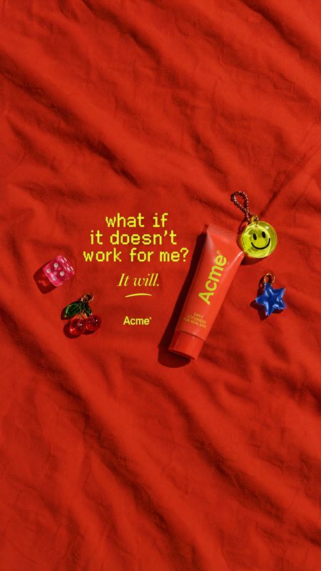 cosmetic tube flat lay product photo: A coral cosmetic tube and playful charms are arranged on rumpled red fabric beside bold yellow copy, creating a vivid, ch…