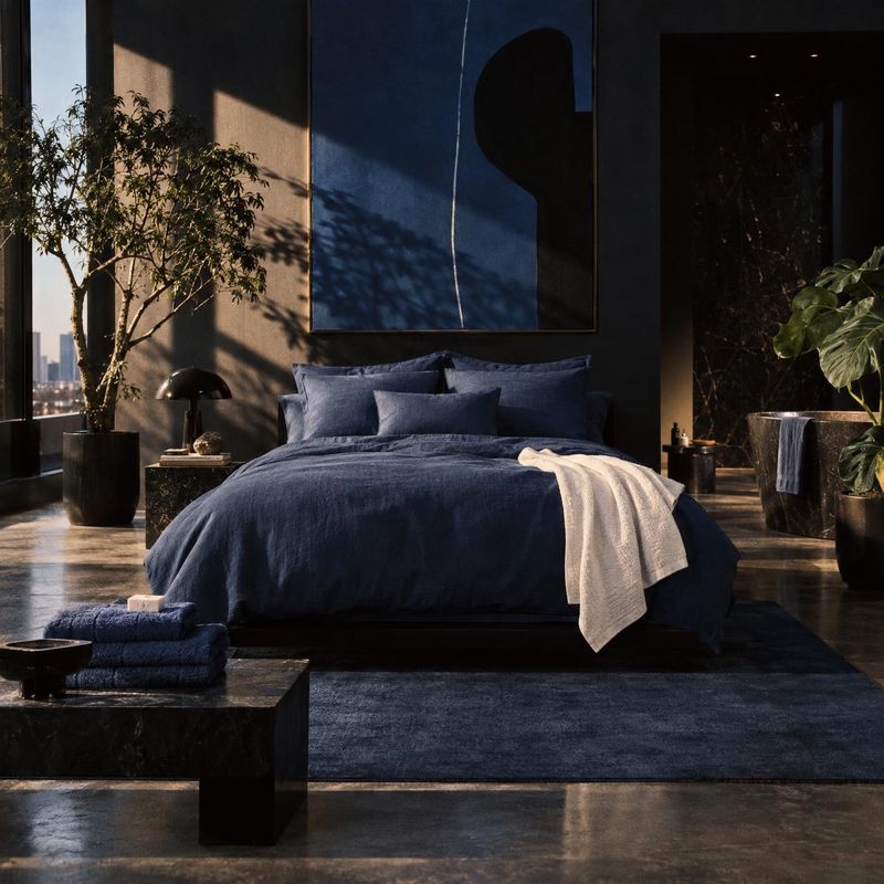 bedding set room set product photo: A navy bedding set anchors a sophisticated bedroom styled with dark stone, leafy plants, abstract wall art, and warm late-a…