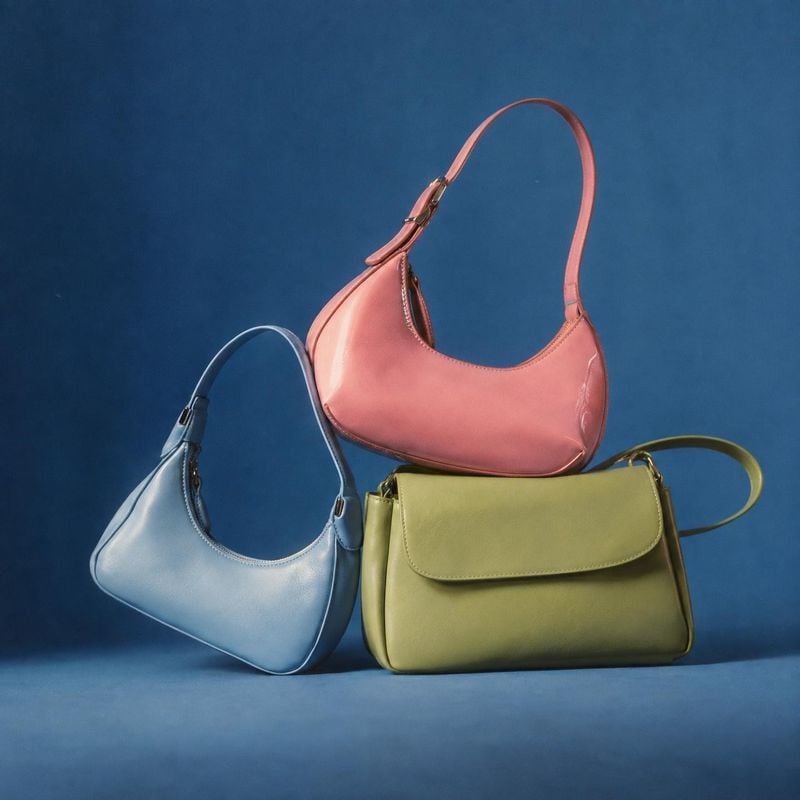 handbags group lineup product photo: Three pastel leather handbags are arranged together against a deep blue studio backdrop, with soft directional lighting cr…