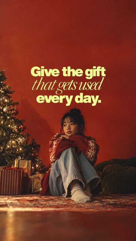 knit sweater christmas product photo: A woman in a patterned red knit sweater sits beside a glowing Christmas tree and wrapped gifts against a warm red backdro…
