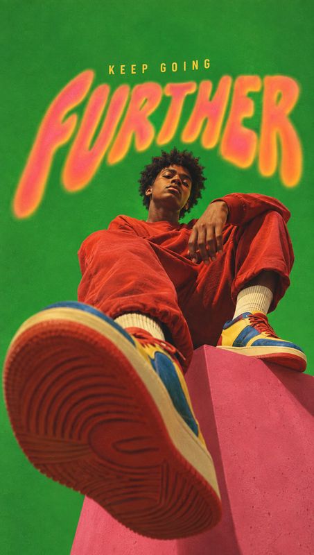 sneakers on-body detail product photo: A low-angle fashion image shows a seated model in a vivid red outfit and colorful sneakers against a saturated green stu…