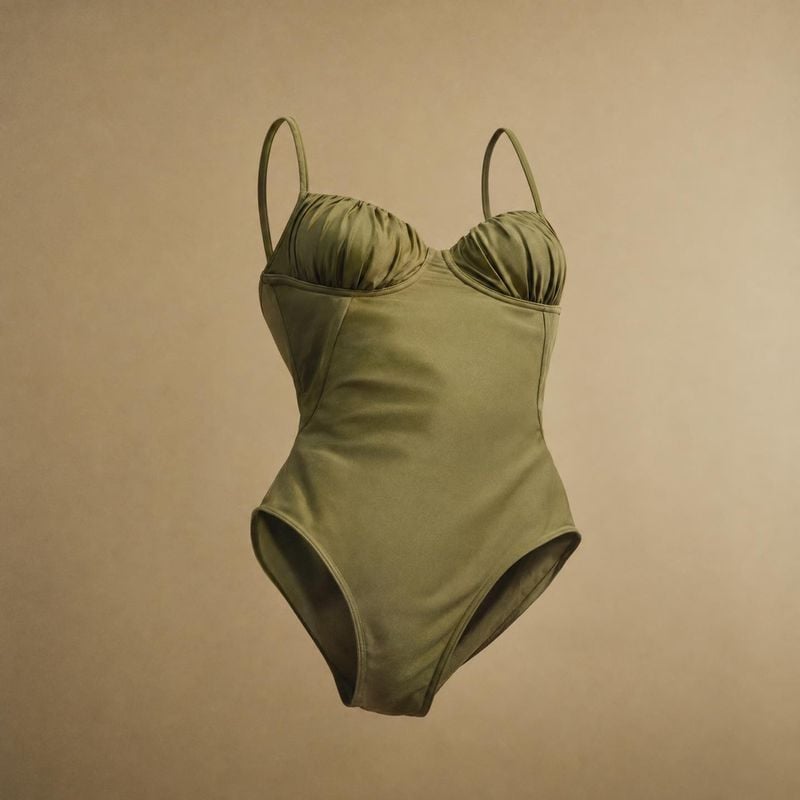 one-piece swimsuit fashion product photo: An olive-green one-piece swimsuit floats against a warm beige studio backdrop, softly lit with a calm, minimal mood.