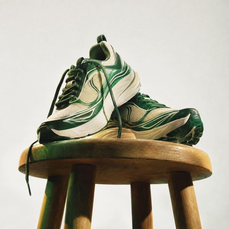 green and cream running sneakers fashion product photo: Two green-and-cream running sneakers are artfully stacked on a rustic wooden stool against a pale studi…