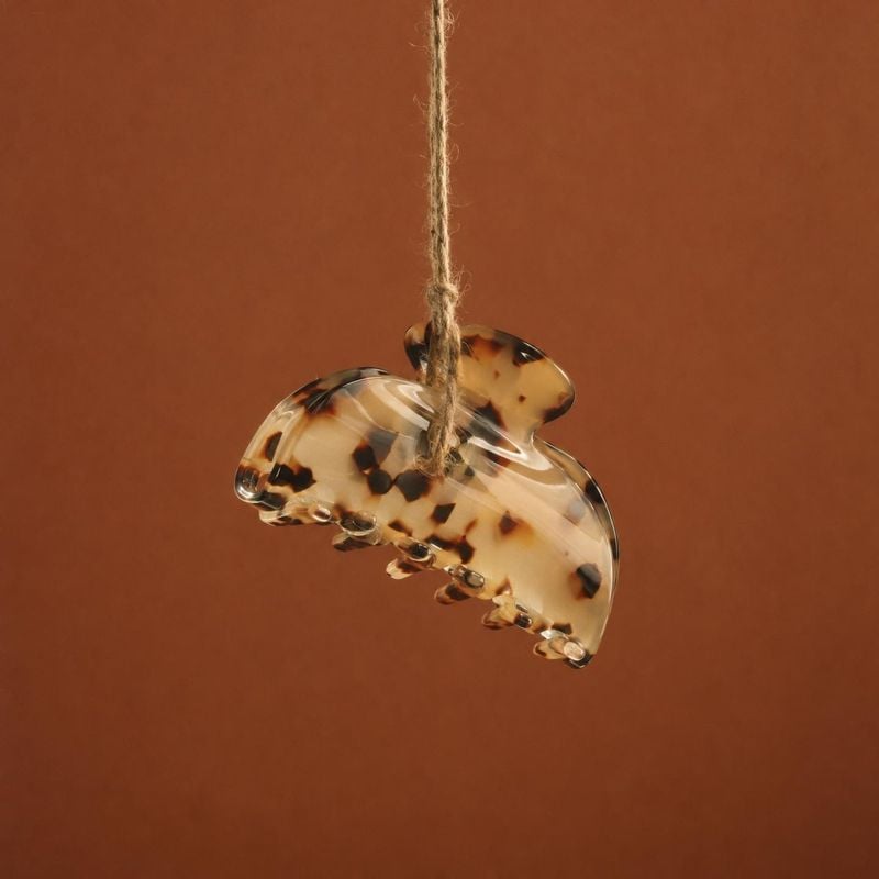 tortoiseshell hair claw clip jewelry product photo: A translucent tortoiseshell-pattern hair claw clip hangs from a rustic cord against a warm terracotta studi…