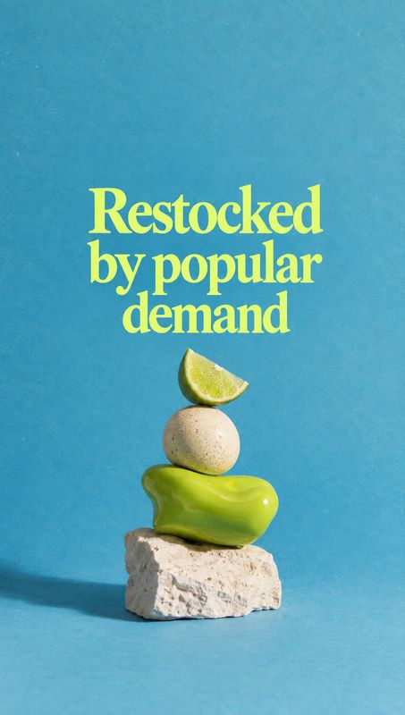 green soap bar still life product photo: A vivid green soap bar is balanced with a stone, a round object and a lime wedge against a bright blue studio backdrop…