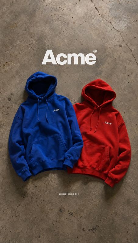 hoodies flat lay product photo: Two brightly colored hoodies are arranged on a textured concrete surface beneath large white brand lettering, with overhead lig…