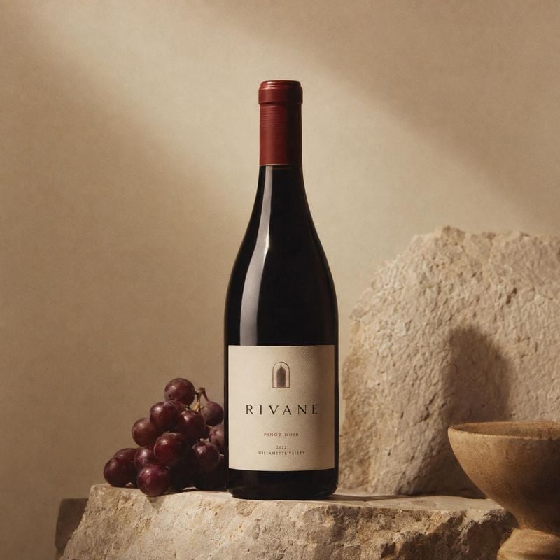 Pinot Noir wine food and drink product photo: A dark wine bottle with a cream label stands beside red grapes and a rustic stone bowl, lit warmly against a text…