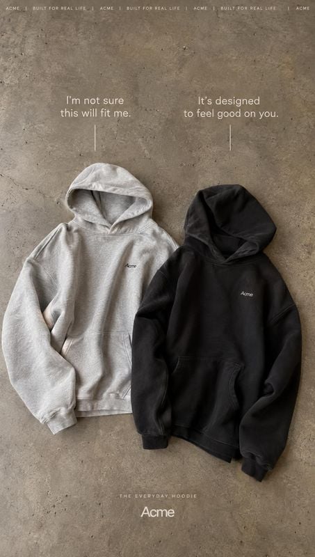 hoodies flat lay product photo: Two hoodies, one light grey and one black, lie on a textured concrete surface beneath understated white promotional copy, creat…
