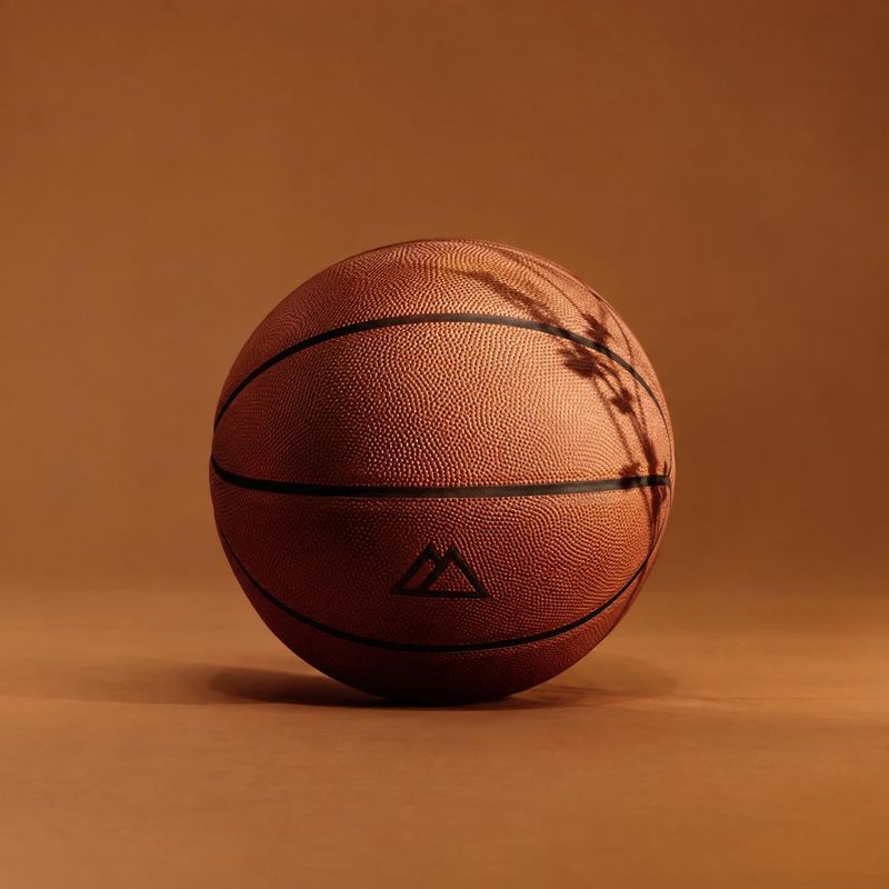 basketball sports product photo: A textured basketball rests centered on a warm brown studio surface, lit with dramatic amber light and a soft shadow for a min…
