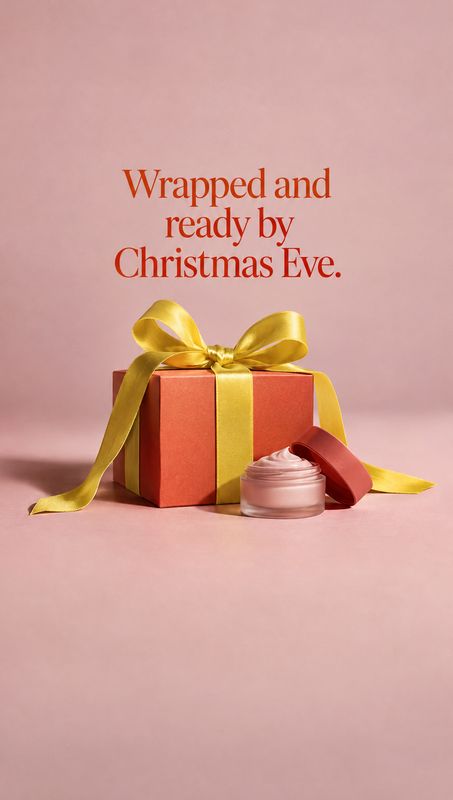 face cream christmas product photo: A pink face cream jar sits beside a coral gift box wrapped with a golden ribbon on a soft pink studio set, beneath a festiv…