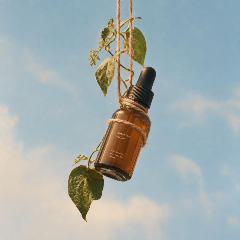 botanical serum floating product product photo: An amber botanical serum bottle hangs among leafy stems against an open blue sky, lit by warm natural sunlight…