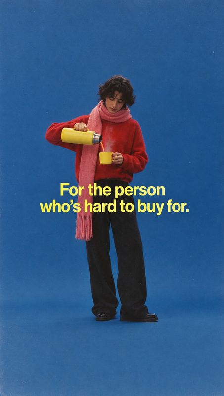 thermos flask and mug product in hand product photo: A person in a red sweater and pink scarf pours from a yellow thermos into a matching mug against a vivid b…