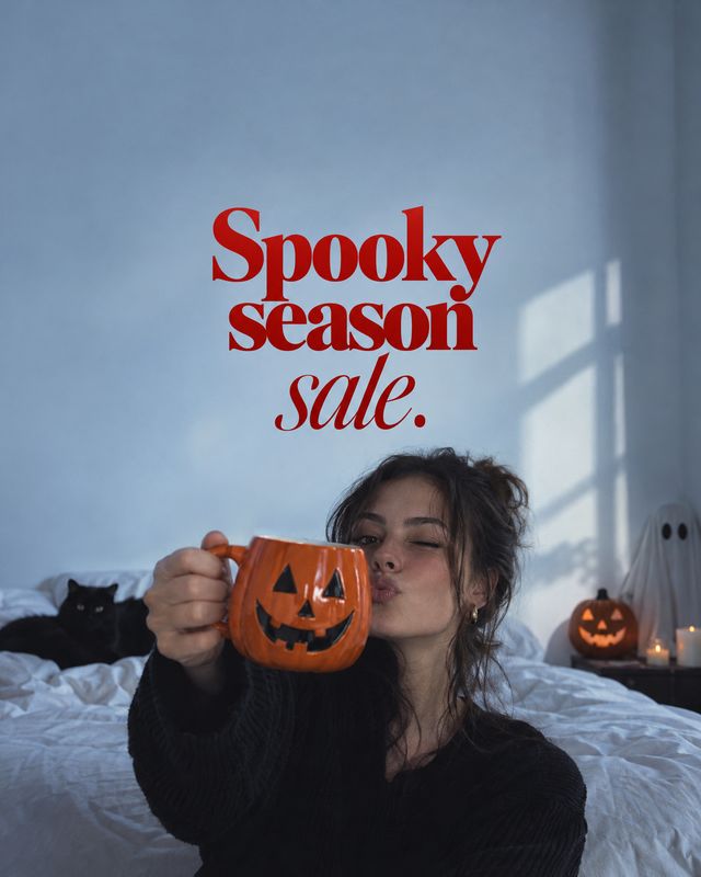 pumpkin mug halloween product photo: A woman in a black sweater raises an orange jack-o'-lantern mug in a softly lit bedroom, with Halloween decorations and bo…