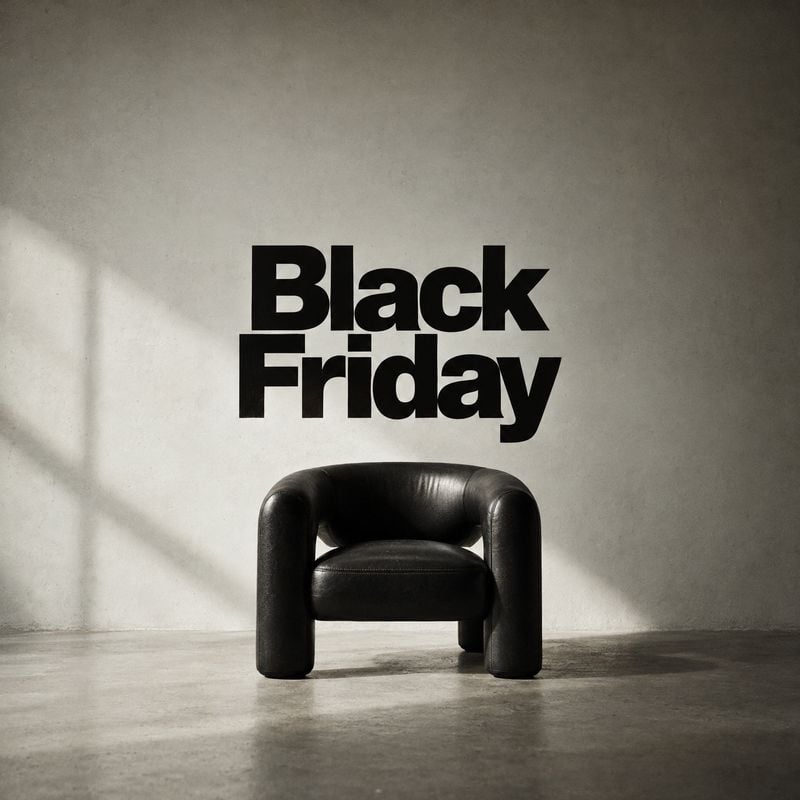 black leather armchair room set product photo: A sculptural black leather armchair sits in a sparse concrete interior beneath bold Black Friday lettering, lit…