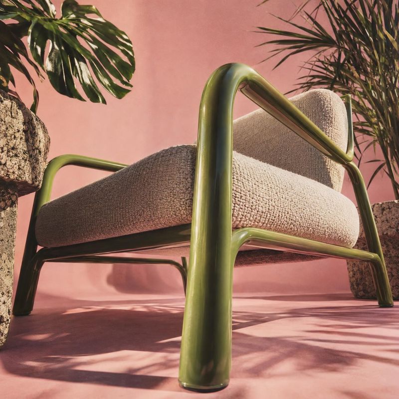 upholstered lounge chair room set product photo: A sculptural lounge chair with plush beige upholstery and glossy green tubular framing is staged against a war…