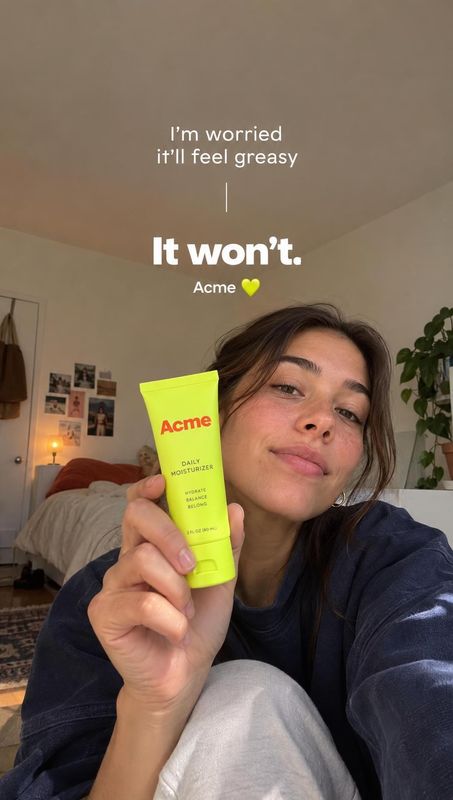 daily moisturizer product in hand product photo: A woman holds a bright lime moisturizer tube close to the camera in a cozy bedroom, with casual selfie styling…