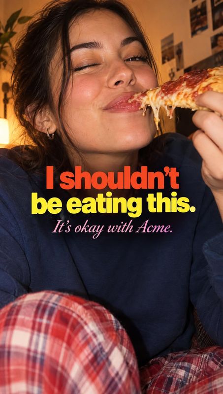 pizza lifestyle scene product photo: A woman in a dark sweatshirt and plaid pants playfully bites a slice of pizza in a warmly lit interior, with bold red and…