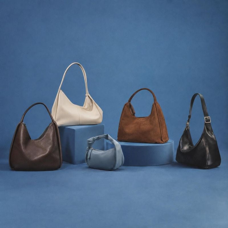 handbags group lineup product photo: Five leather handbags in varied colors and shapes are arranged on blue display plinths against a matching blue studio back…