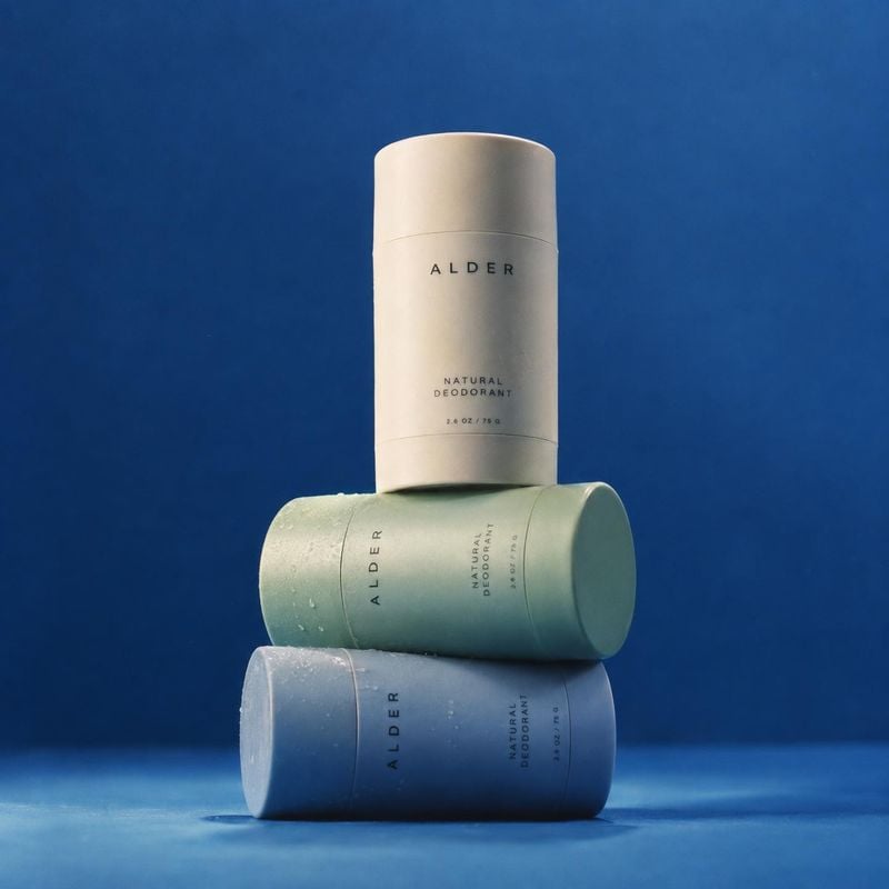 natural deodorant group lineup product photo: Three Alder natural deodorant sticks in cream, sage, and blue are stacked against a vivid blue studio backdrop, w…