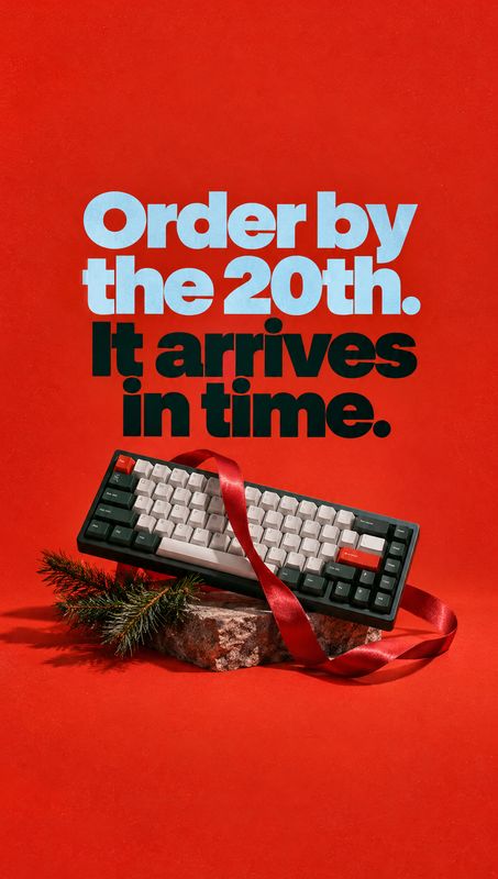 mechanical keyboard electronics product photo: A compact mechanical keyboard rests among evergreen sprigs and a red ribbon on a vivid red studio set, beneath b…