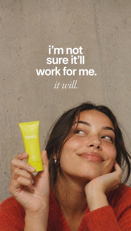 skincare tube product in hand product photo: A woman in a red knit top holds a bright yellow skincare tube beside her face against a warm concrete backdrop, wi…