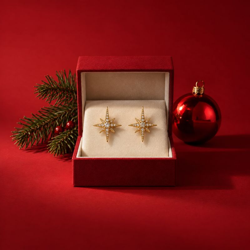gold starburst earrings christmas product photo: A pair of gold starburst earrings with clear stones sits in an open red velvet box beside evergreen sprigs and…