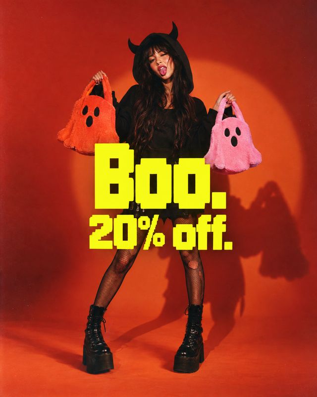 plush ghost handbags halloween product photo: A woman in a black devil-inspired outfit holds orange and pink ghost handbags against a vivid red-orange studio b…