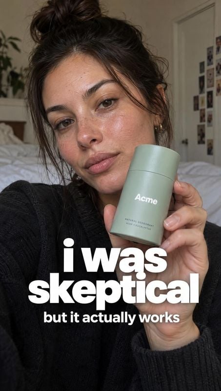 natural deodorant personal care product photo: A woman in a black knit top holds a pale green deodorant toward the camera in a softly lit bedroom, while bold w…