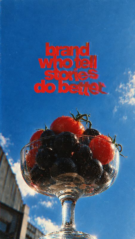 assorted fruit ingredients product photo: A glass bowl of glossy tomatoes and dark berries is photographed from a low angle against a vivid blue urban sky, wit…
