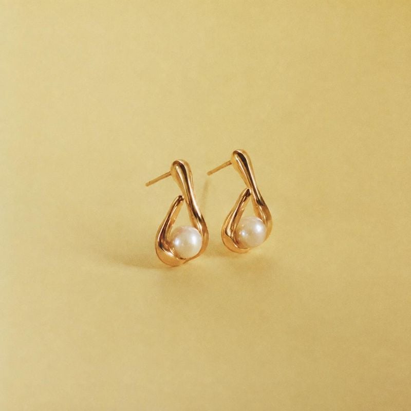 pearl earrings jewelry product photo: A pair of gold-tone earrings with luminous pearl accents is centered against a warm yellow backdrop, lit softly for a cle…