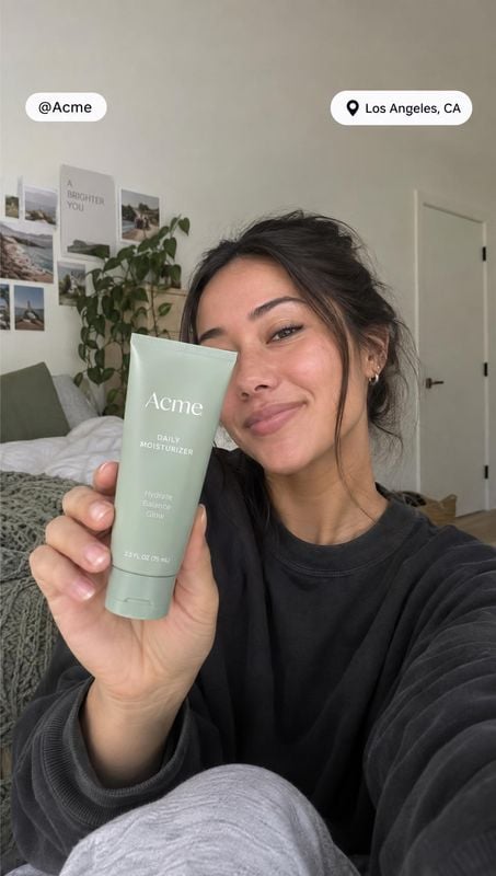 daily moisturizer product in hand product photo: A woman holds a pale green moisturizer tube close to the camera in a cozy bedroom, with soft natural light and…