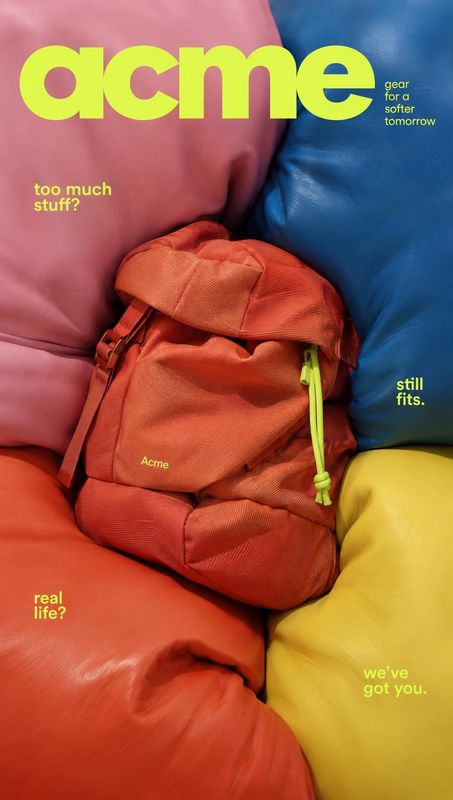 backpack jewelry product photo: A burnt-orange backpack is nestled among oversized pink, blue, red, and yellow padded forms, with vivid lime typography and a p…