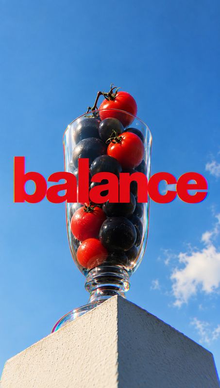 tomatoes food and drink product photo: A glass filled with red and dark tomatoes balances atop a pale stone pedestal against a vivid blue sky, with bold red “b…