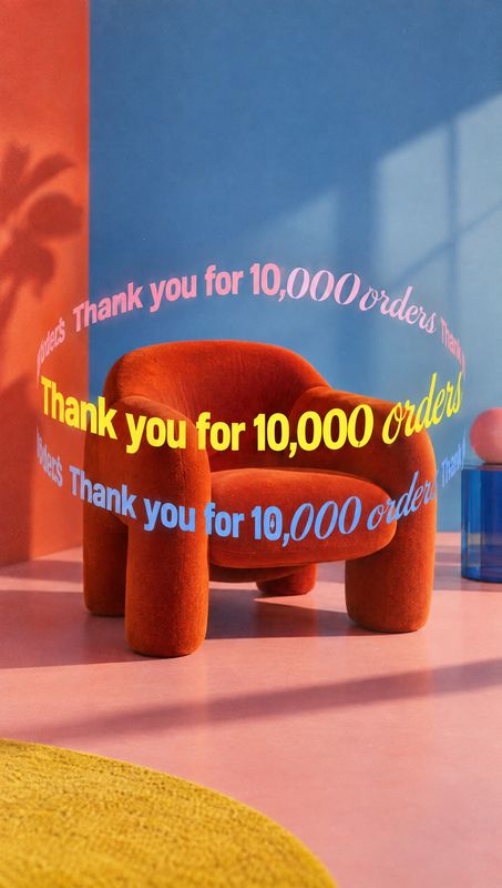 upholstered chair room set product photo: A sculptural rust-red upholstered chair sits in a vivid blue-and-pink interior, wrapped in curved yellow and pastel l…