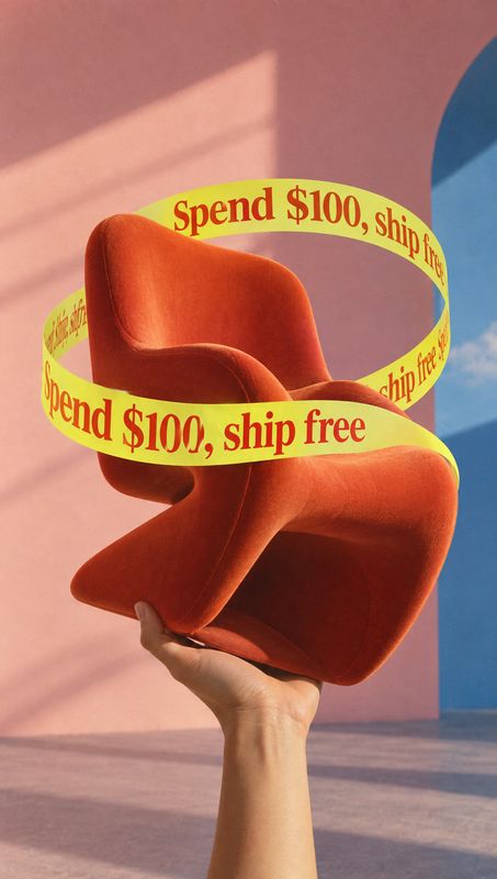 upholstered chair product in hand product photo: A sculptural orange upholstered chair is held aloft by a hand against a sunlit pink-and-blue studio set, wrapp…
